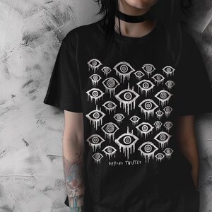 May include: Black t-shirt featuring a white graphic print of repeating stylised eyes with dripping lines. The text "Beyond Twisted" is printed below the graphic.
