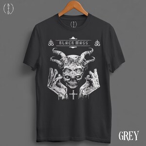May include: A charcoal grey short-sleeve t-shirt featuring a white graphic print of a horned skull flanked by two hands. The text "BLACK MASS" is printed above the skull, accompanied by two cross symbols and a small cross below the chin.