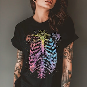 May include: A black t-shirt with a rainbow-colored ribcage graphic. The graphic is a stylized anatomical illustration of a human ribcage.