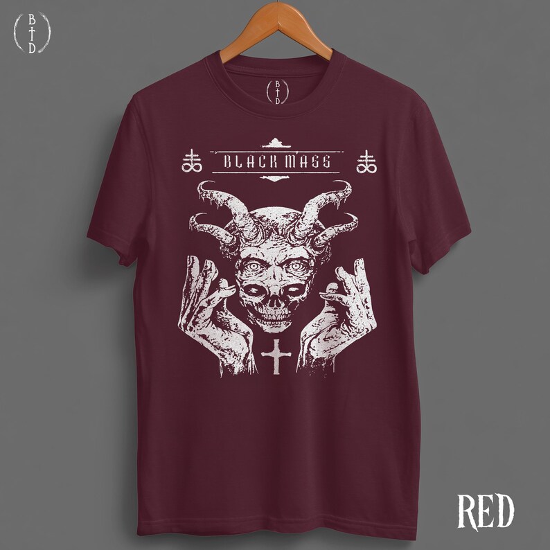 May include: A maroon short-sleeve t-shirt featuring a white graphic print of a horned skull with hands raised on either side. The text "BLACK MASS" is printed above the skull, flanked by two cross symbols. A small cross is centered below.