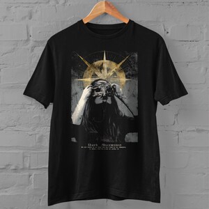 Puede incluir: Camiseta negra con un dise&ntilde;o gr&aacute;fico de una mujer con m&aacute;scara, una forma dorada similar a una br&uacute;jula y el texto "Dark Ascension". El dise&ntilde;o tiene un aspecto vintage y desgastado.