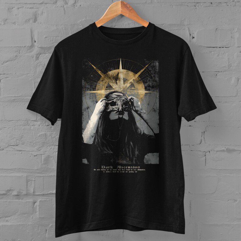 Puede incluir: Camiseta negra con un dise&ntilde;o gr&aacute;fico de una mujer con m&aacute;scara, una forma dorada similar a una br&uacute;jula y el texto "Dark Ascension". El dise&ntilde;o tiene un aspecto vintage y desgastado.