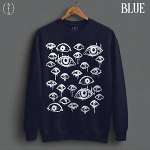 May include: A navy blue crewneck sweatshirt featuring a white graphic print of numerous eyes of varying sizes. Many of the eyes have a dripping effect. The word BLUE is printed in the top right corner, and a BTD logo is in the top left.