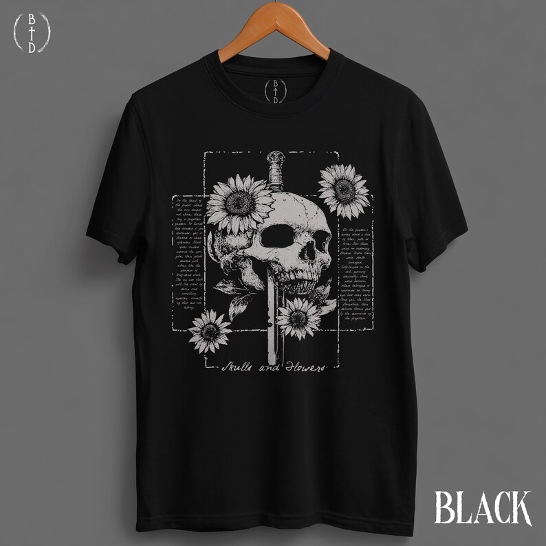 May include: Black t-shirt featuring a detailed skull pierced by a sword, surrounded by sunflowers. The design includes the text "Skulls and Flowers" and a rectangular frame with text. The word "BLACK" is printed at the bottom right.