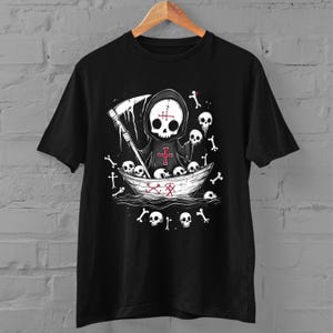 May include: Black t-shirt with a graphic of a skeleton wearing a hooded robe and holding a scythe. The skeleton is in a boat with skulls and bones around it. The text "X" is on the boat.