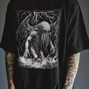 K&ouml;nnte beinhalten: Schwarzes T-Shirt mit einem wei&szlig;en Grafikdruck eines Cthulhu-&auml;hnlichen Wesens mit Tentakeln, die aus dem Wasser ragen.
