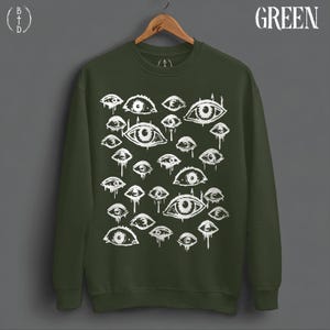 May include: A dark olive green crewneck sweatshirt featuring a repeating white graphic print of various stylized eyes with dripping details. The word GREEN is printed in white in the top right corner, and a BTD logo is in the top left.