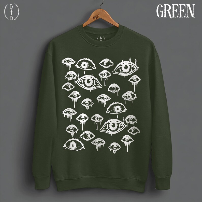 May include: A dark olive green crewneck sweatshirt featuring a repeating white graphic print of various stylized eyes with dripping details. The word GREEN is printed in white in the top right corner, and a BTD logo is in the top left.