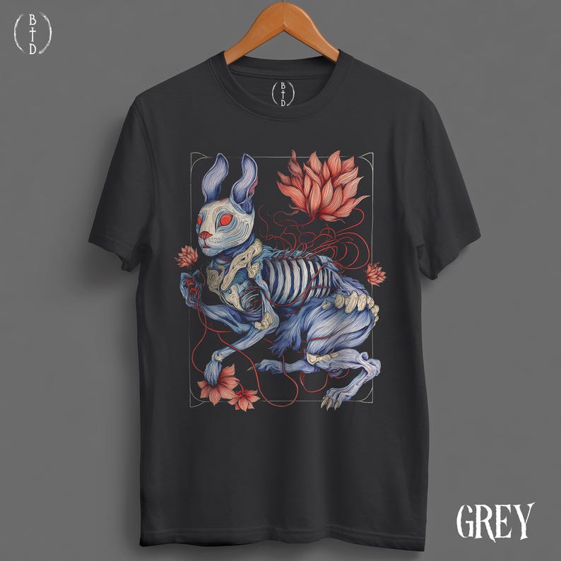 May include: Dark grey t-shirt featuring a detailed illustration of a rabbit with exposed skeletal structure, red eyes, and floral accents. The design is framed within a white border, with the word "GREY" printed at the bottom.