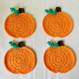May include: Four orange crochet pumpkin coasters with green vines and brown stems. These handmade coasters are perfect for fall decor and add a touch of autumn to any home. Each coaster is approximately 4 inches in diameter.