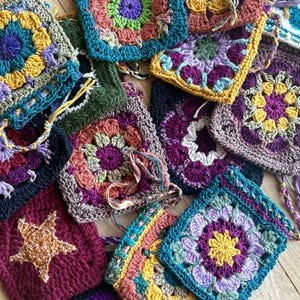 Puede incluir: Una colección de cuadrados de ganchillo hechos a mano y coloridos en varios tonos de morado, verde, amarillo y azul. Algunos cuadrados presentan diseños de estrellas y medias lunas. Los cuadrados están dispuestos juntos, mostrando el intrincado trabajo de puntadas y las vibrantes combinaciones de colores.