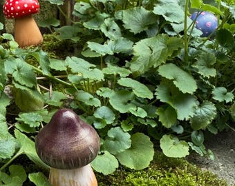 May include: Two ceramic mushrooms, one red with white dots and one brown with gold accents, are nestled in a bed of green moss and leaves.
