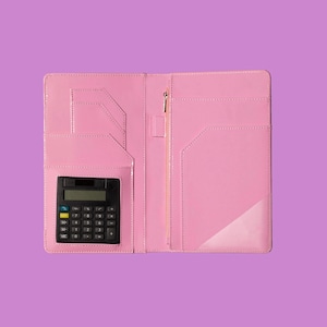 Op de afbeelding: Open roze kunstleren business organizer met een zwarte rekenmachine. De organizer heeft meerdere vakken, een vak met ritssluiting en een pennenhouder. De rekenmachine zit in de linker onderzak.