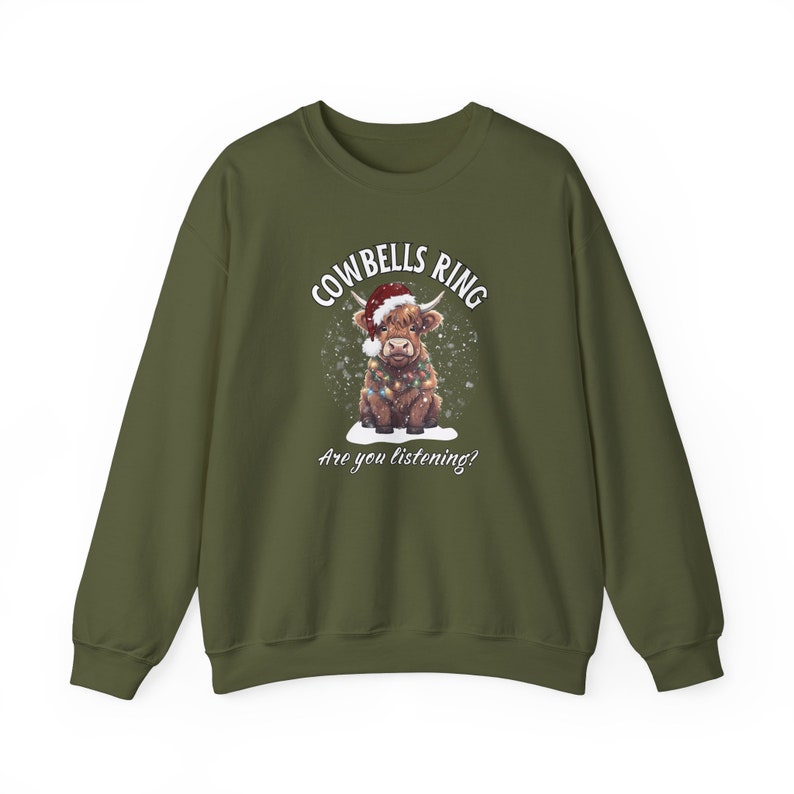 May include: Olive green sweatshirt featuring a festive Highland cow illustration. The cow wears a Santa hat and Christmas lights, with the text "Cowbells Ring, Are you listening?" in white. A cozy, seasonal design.