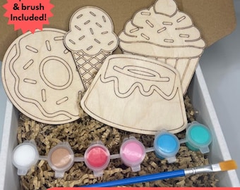 May include: A kids' paint kit with four wooden dessert shapes: a donut, ice cream cone, cupcake, and pudding. The kit includes six paint colors, a paintbrush, and the text "4 Piece Kids Paint Kits". The box also says "6 paints & brush Included!"