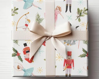 May include: White gift wrap with a repeating pattern of nutcrackers, ballerinas, snowflakes, and holly. A cream-colored ribbon is tied in a bow on top of the wrapping paper.