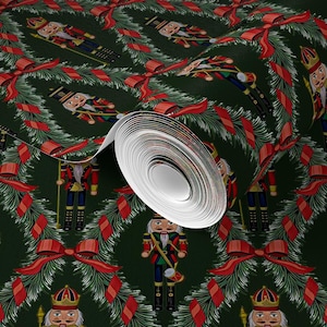 Op de afbeelding: Rol behang met een herhalend patroon van kerstnotenkrakers, rode strikken en groene kransen. De notenkrakers staan in verschillende poses, gekleed in rode, blauwe en gouden uniformen. De achtergrond is donkergroen.
