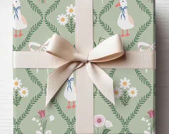 Puede incluir: Una caja de regalo envuelta con papel estampado verde claro. El patrón incluye margaritas blancas, gansos con lazos azules y detalles florales. Una cinta y un lazo color crema están atados alrededor de la caja, creando una presentación clásica y elegante.