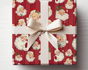 Op de afbeelding: Een ingepakte geschenkdoos met rood inpakpapier met een patroon van Sinterklaasgezichten. Een crèmekleurig lint en strik zijn om de doos gebonden. De achtergrond is een wit houten oppervlak.