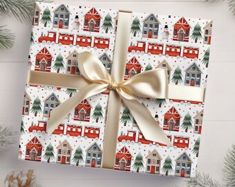May include: A wrapped gift with festive Christmas-themed wrapping paper. The paper features a repeating pattern of red houses, green trees, and red trains on a white background. A gold ribbon and bow secure the gift.