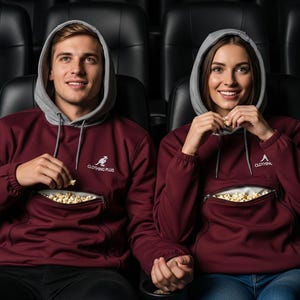 Op de afbeelding: Twee mensen dragen bordeauxrode hoodies met grijze capuchons en kangoeroezakken gevuld met popcorn. De hoodies hebben de tekst "CLOTHING PLUS" en "CLOTHING" erop gedrukt. Ze zitten in een bioscoop.