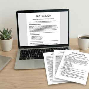 May include: A silver laptop displaying a resume for Brie Hamilton, an Advanced Care Paramedic. Three printed copies of the same resume are stacked in the foreground. The resume includes sections for Professional Summary and Core Competencies.
