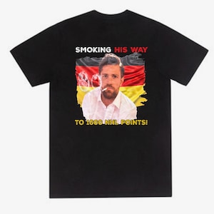 Könnte beinhalten: Schwarzes T-Shirt mit einer Grafik eines Mannes, der vor einer deutschen Flagge eine Zigarette raucht. Der Text lautet: "SMOKING HIS WAY TO 1000 NHL POINTS!"