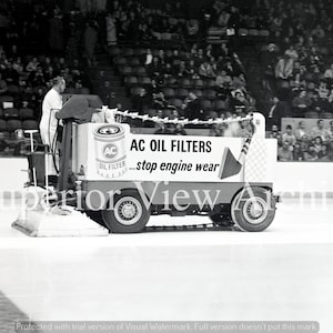 Könnte beinhalten: Schwarz-Weiß-Foto einer Eismaschine mit dem Text "AC OIL FILTERS...stop engine wear". Die Maschine hat das Logo "AC OIL FILTER". Eine Person bedient die Maschine auf einer Eisbahn, mit Zuschauern im Hintergrund.
