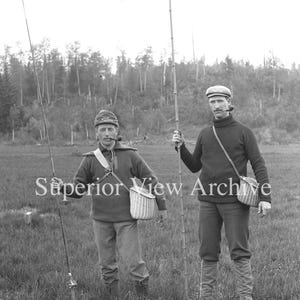 Puede incluir: Fotografía en blanco y negro de dos hombres en un campo, cada uno sosteniendo una caña de pescar. Llevan sombreros, suéteres y cestas de mimbre. El texto "Superior View Archive" es visible.