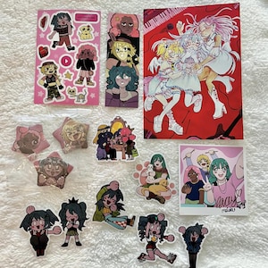 May include: A collection of anime-style stickers and art prints featuring various characters with colorful hair, including a pink sticker sheet, a vertical bookmark, a large red print, star-shaped badges, and a square print signed with the text lacey.