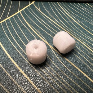 May include: Two white plastic spools of thread, one slightly larger than the other, on a textured surface.