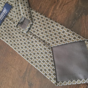 May include: A necktie featuring a repeating geometric pattern of interlocking circles in olive green, light blue, and white. The tie includes a dark blue label with the white text STAFFORD MADE IN ITALY and a smaller black care tag.