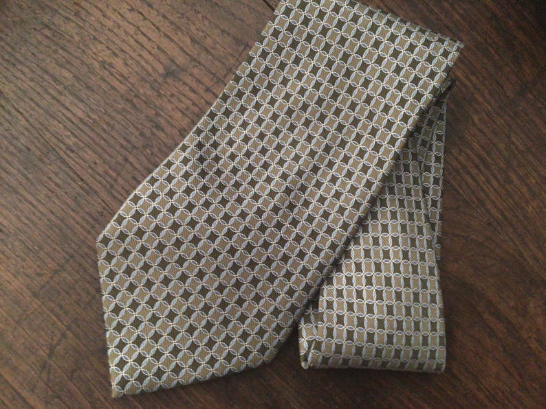 May include: A necktie featuring a repeating geometric pattern of interlocking circles and ovals in shades of olive green, tan, and white. The fabric has a subtle sheen, and the design is consistent across the entire surface of the folded necktie.