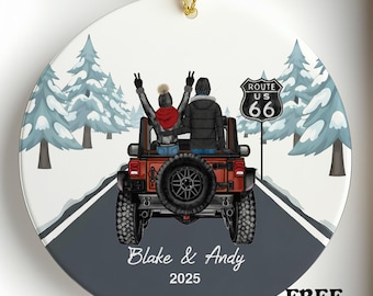 May include: A round ceramic ornament featuring a couple in a red Jeep on a road with snow-covered trees. The ornament has the text "Route 66", "Blake & Andy 2025", and "SALE". A gold string is attached for hanging.
