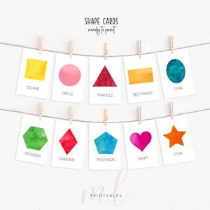 May include: Ten cards displaying various shapes in watercolour, including a square, circle, triangle, rectangle, oval, hexagon, diamond, pentagon, heart, and star. The cards are suspended from a string with pegs. Text on the cards reads "SHAPE CARDS ready to print".