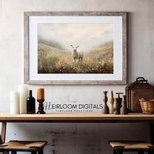 May include: A framed print of a lamb standing in a field of wildflowers. The artwork is in a rustic, weathered gray frame. The print has a soft, pastel color palette with a dreamy, pastoral feel. The text "Heirloom Digitals" is visible.