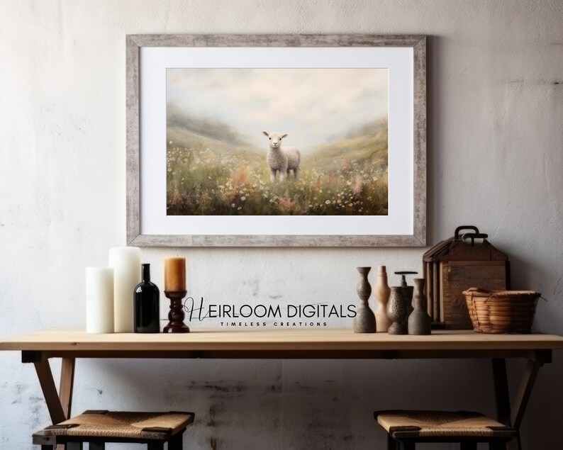 May include: A framed print of a lamb standing in a field of wildflowers. The artwork is in a rustic, weathered gray frame. The print has a soft, pastel color palette with a dreamy, pastoral feel. The text "Heirloom Digitals" is visible.