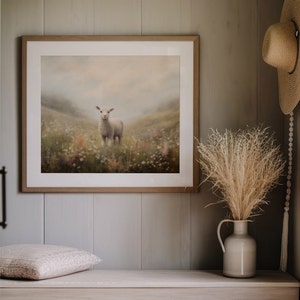 May include: A framed artwork featuring a lamb standing in a field of wildflowers. The artwork is in a light wood frame and hangs on a gray wall. A straw hat and a vase with dried grasses are also visible.