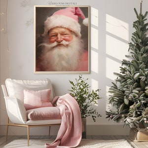 May include: A framed painting of Santa Claus with a pink hat and beard. He is smiling and has a rosy complexion. The painting is hanging on a white wall in a room with a pink armchair, a potted plant, and a decorated Christmas tree.