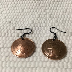 May include: A pair of copper coin earrings with black hooks. The coins feature a design of a bird with the number 25 on the front.