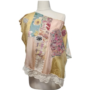 May include: A sleeveless top constructed from patchwork fabric panels in shades of yellow, pink, and blue. The garment features a printed eye motif, floral patterns, a textured pink embroidered section, and a white scalloped lace trim along the hem.
