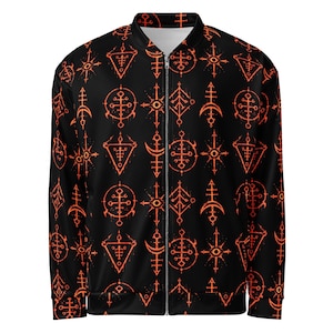 May include: A black bomber jacket featuring a repeating pattern of orange symbols, including stylised crosses, crescents, and eye motifs. The jacket has a full-length silver zip down the centre front, long sleeves, and a ribbed collar.