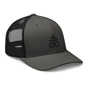 May include: A dark gray trucker hat with a black mesh back. The hat features a black embroidered symbol of a cross with a circle around it.