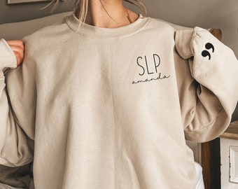 Puede incluir: Una sudadera beige con el texto "SLP amanda" y comillas en las mangas.