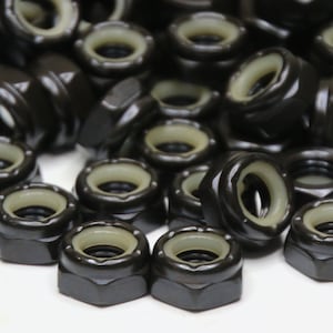 Op de afbeelding: Een verzameling zwarte borgmoeren met een nylon inzetstuk en een lichtgroen interieur. De moeren zijn zeshoekig en hebben een glanzende afwerking. De afbeelding toont een close-up van de hardware.
