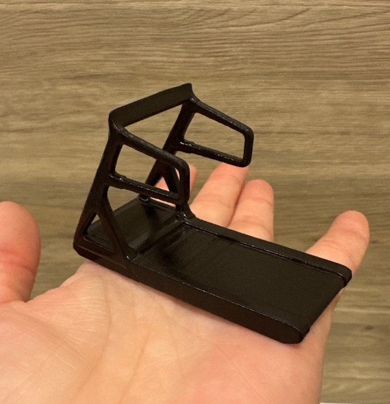 Może przedstawiać: Czarny model miniaturowej bieżni. Bieżnia ma czarną ramę i czarną powierzchnię biegową.
