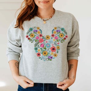 a woman wearing a mickey mouse sweatshirt with flowers on it