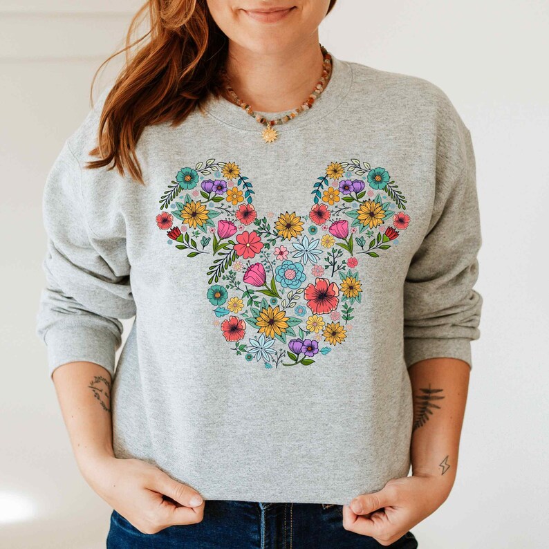 a woman wearing a mickey mouse sweatshirt with flowers on it