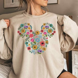 a woman wearing a mickey mouse sweatshirt with flowers on it