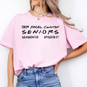 May include: Pink t-shirt with the text "Our Final Chapter Seniors Season:20 Episode:24" in black.